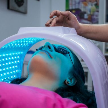 Unrecognizable woman with dark hair with pierced ears lying under ultraviolet lamp while visiting contemporary clinic and spending time in modern salon